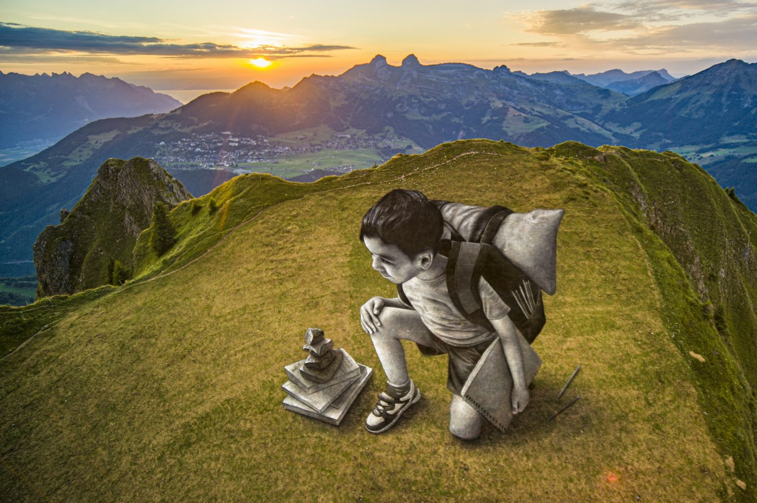 A boy with art supplies rests on a mountaintop while looking at another mountain in front of a sunrise.